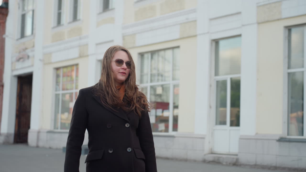 Station light beams softly behind lady sitting on city bench using phone near red structure and classic brick buildings, capturing warm evening ambiance, and quiet interaction within urban atmosphere