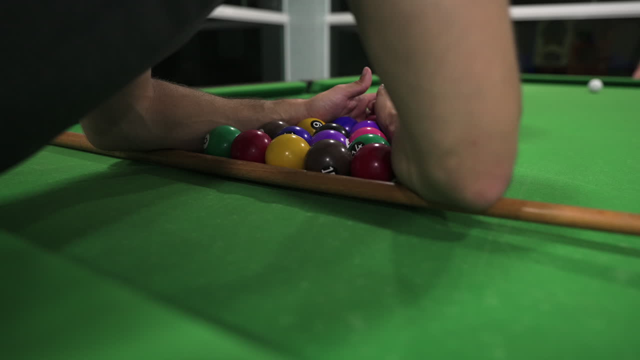 Close-up view of person arranging colorful pool balls into a tight triangle after the break time