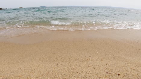 a steady camera close-up shot of sea waves crashing on a sandy beach on a sunny summer day in the mediterranean