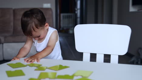 cute little baby boy is tired of playing puzzles. kid stands up from a desk and jumps excitedly.