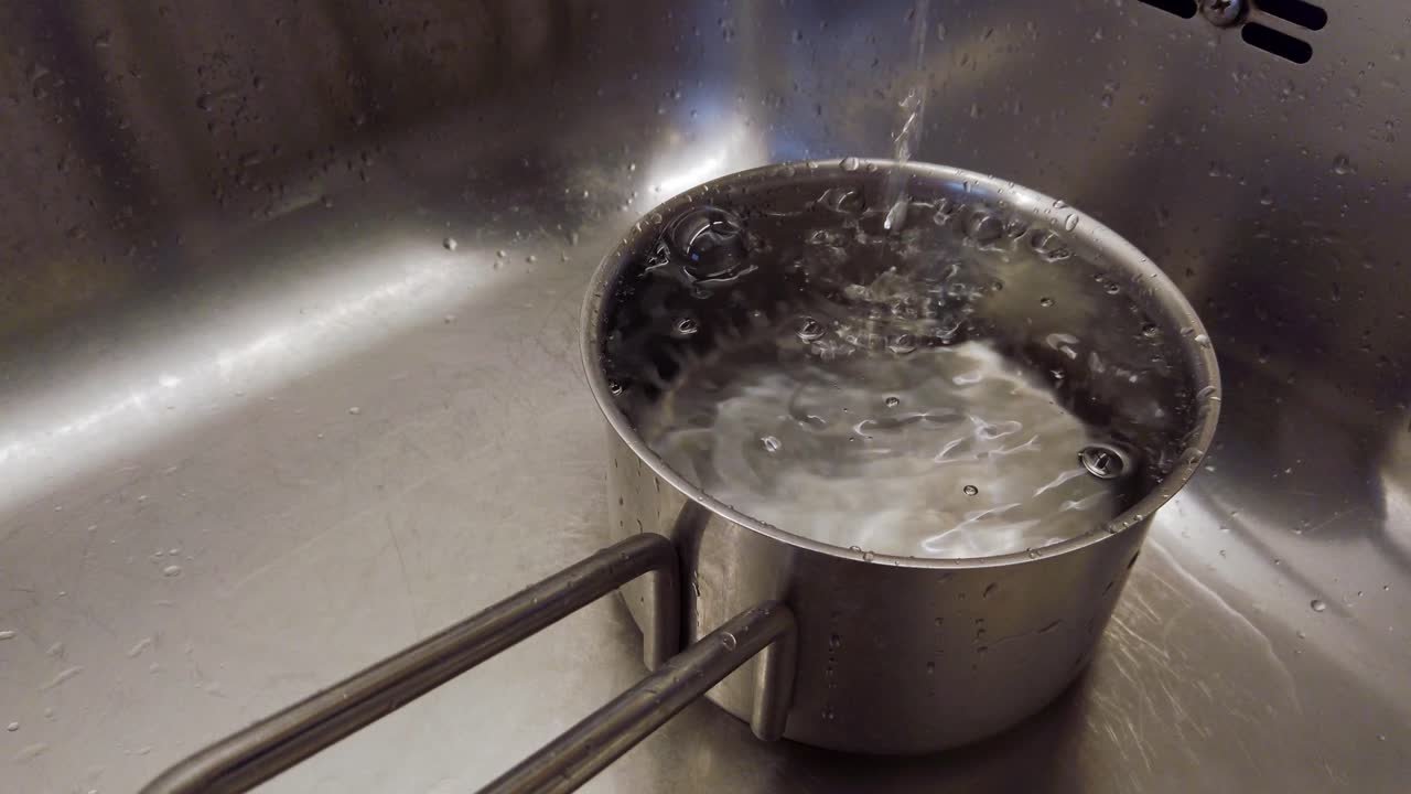 Acqua corrente dal rubinetto in una pentola d'acciaio, bolle sulla superficie dell'acqua
