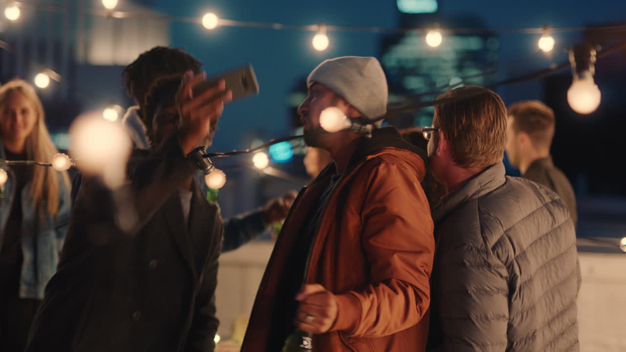 feliz fiesta en la azotea amigos divirtiéndose joven hombre afroamericano tomando fotos usando teléfono inteligente compartiendo el estilo de vida del fin de semana en las redes sociales por la noche