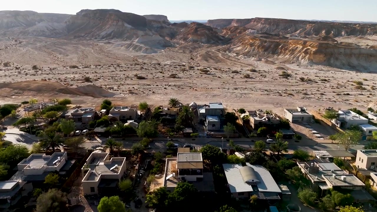 4K 60fps drone footage flying westward over Zukim, Israel, showcasing spectacular golden hour illumination across the rugged Arava Desert landscape, cliffs and surrounding wilderness