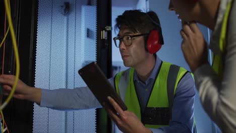 Diverse-female-and-male-it-technicians-wearing-headphones-using-tablet-checking-computer-server