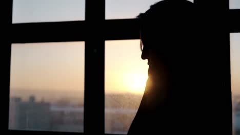 Silhouette-Einer-Dame,-Die-Am-Fenster-Gegen-Sonnenuntergang-Steht