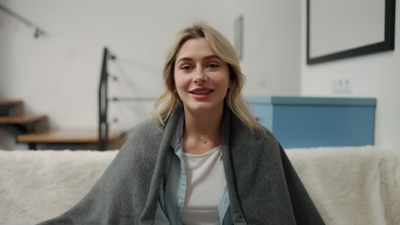 Young smiling woman sitting at home covered in blanket talking to the camera. Vlog, diary and freelancer concept