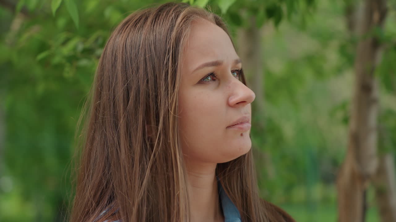retrato de perfil de una mujer caucásica en un parque, vista lateral cerca de árboles frondosos, contemplación tranquila, follaje suavemente iluminado por el sol, expresión serena, tonos naturales, ambiente tranquilo, retrato en primer plano, ambiente veraniego