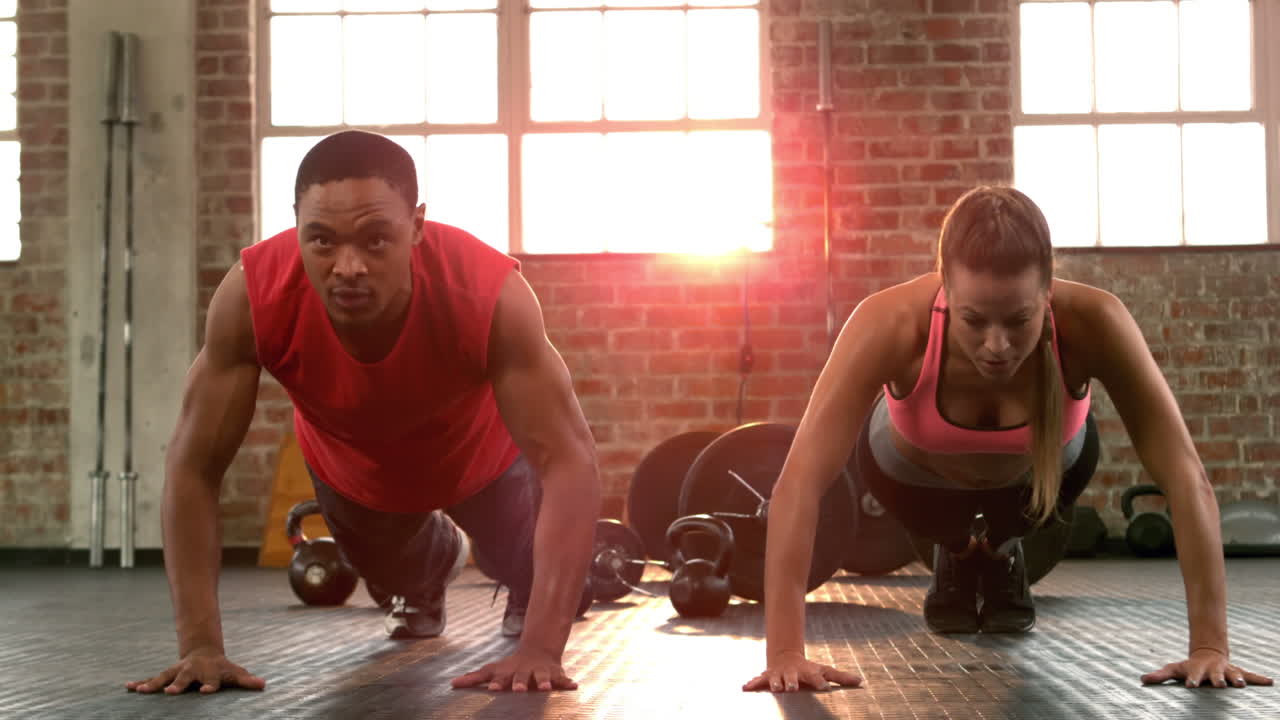 Fit couple doing push ups together in gym 