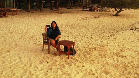 beautiful woman taking selfies and sitting on the sandy shore of an exotic beach island paradise