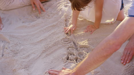 happy family playing on the beach drawing in the sand at sunset