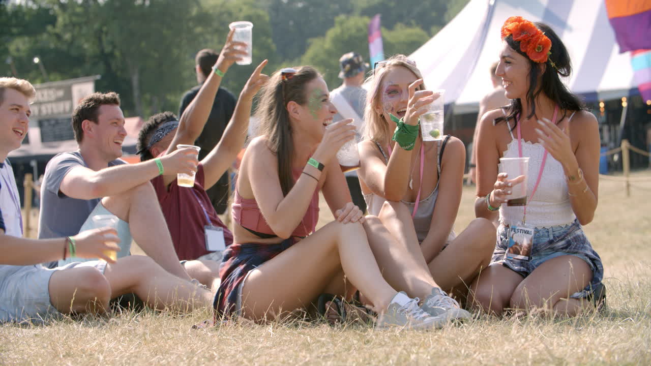 친구 들 이 잔디 에 앉아 음악 축제 에서 공연 을 보고 있다