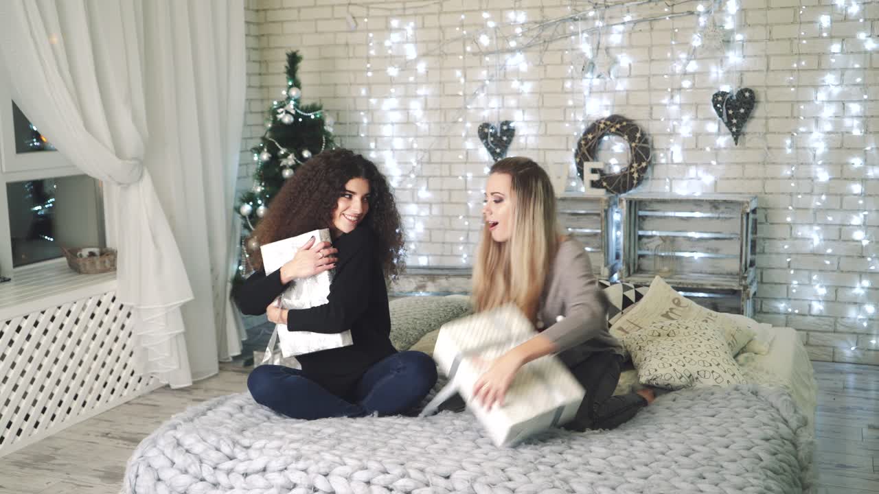 Spirit of Christmas and New Year. Beautiful women with gift sitting on bed next to Christmas tree