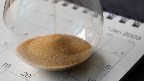 Hourglass-on-table,-sand-flowing-through-the-bulb-of-sandglass