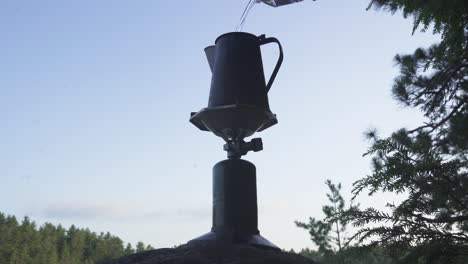 pouring water into stove in wilderness for coffee preparation. surrounded by forest