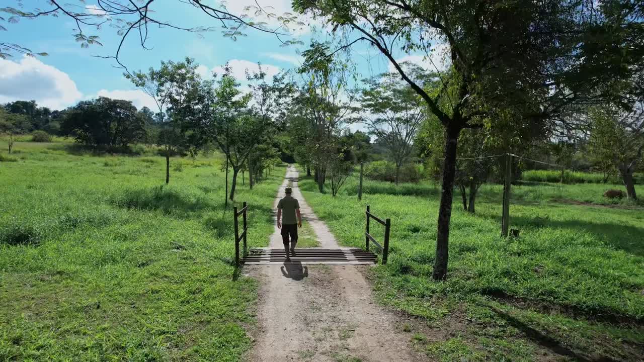 Aerial tracking shot of man walking on dirt trail in countryside, Brazil. Back view