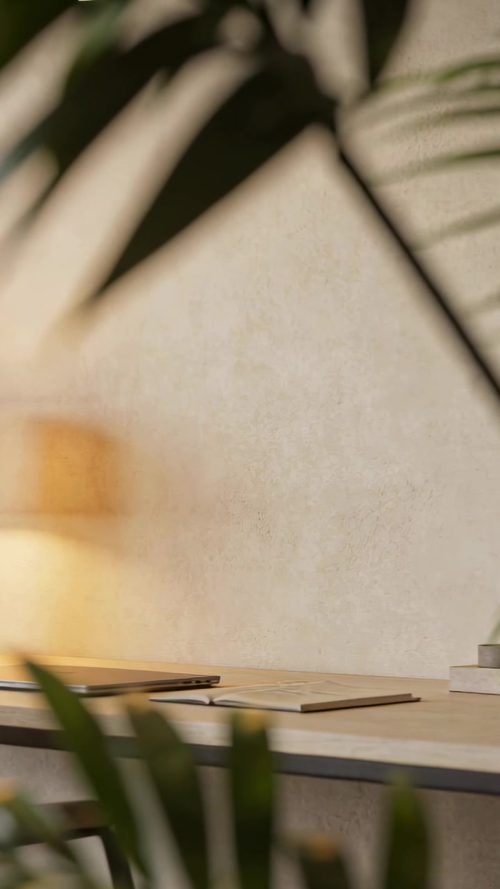 Vertical video: Framing desk with lit lamp and closed laptop at home office, plant fronds shifting
