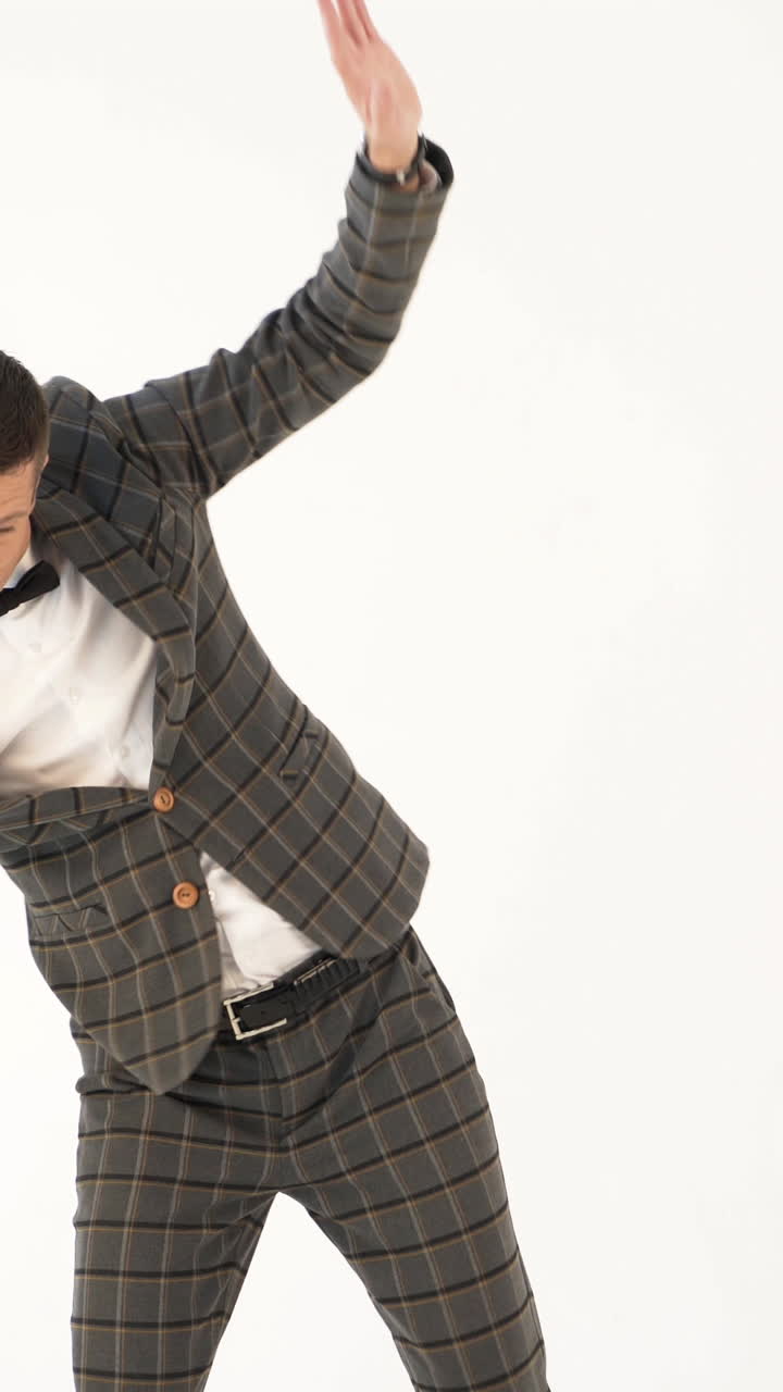 a showman in a plaid suit and white shirt is parodying a businessman with his manners on a white background in the studio Vertical video