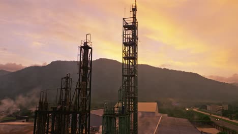 Torre-De-Acero-De-Una-Planta-Industrial-Al-Amanecer-Con-Montañas-Al-Fondo