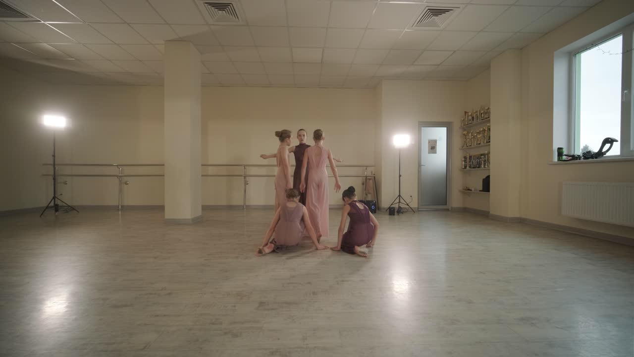 группа молодых студентов балета в черной танцевальной одежде практикует позиции в просторной балетной студии с деревянным полом и настенными решетками. сосредоточенные выражения и синхронизированные движения.