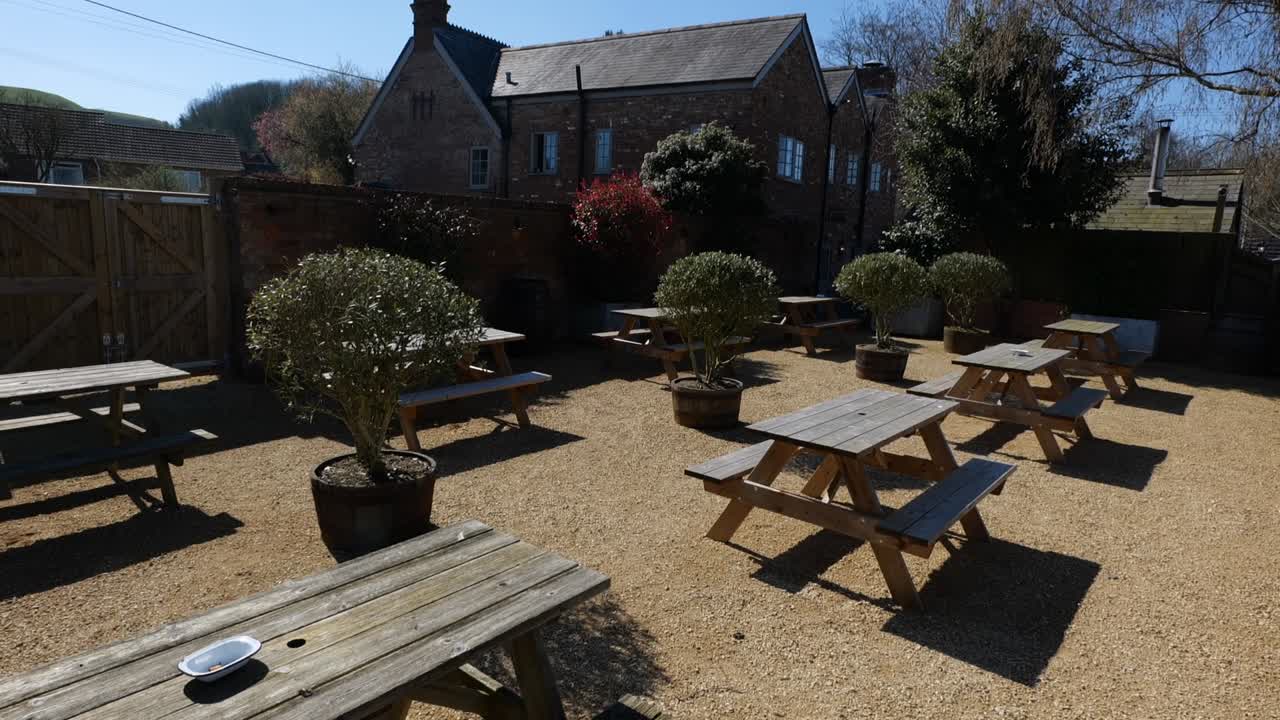 Inquadratura ampia di un giardino di pub vuoto pieno di panchine in una giornata di sole.