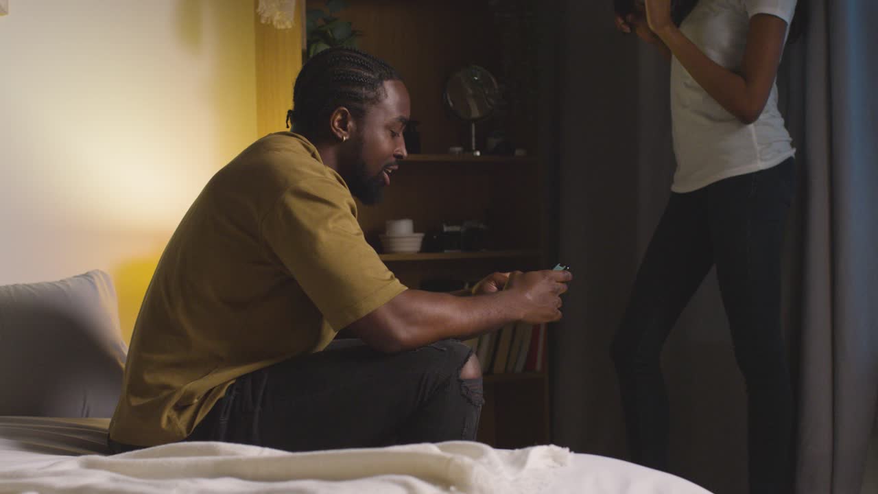 pareja joven relajándose en casa por la noche con un hombre navegando por internet en el teléfono móvil hablando con una mujer 1