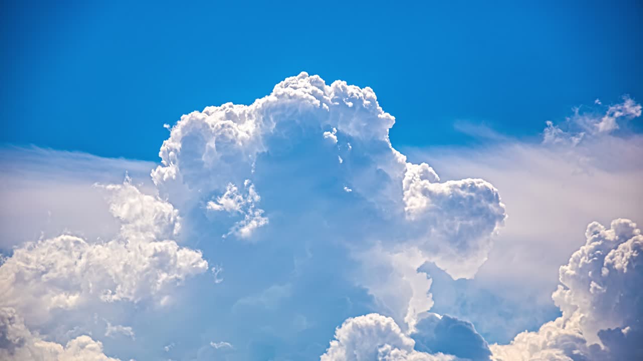 Timelapse of towering cumulus cloud formation growing in a bright blue sky with evolving cloud structure, dynamic atmosphere, shifting weather pattern and dramatic cloudscape above a calm landscape