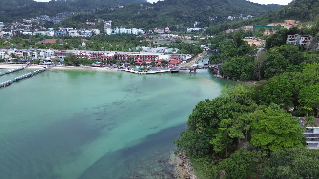 Dynamic drone shot flying fast forward and panning upwards over a bridge and beach in Patong, Phuket, Thailand. Epic tropical coastal view in motion.
