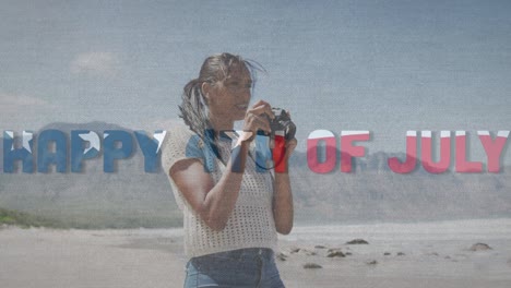 animation of text independence day over african american woman taking photo at beach