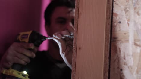 interior work in progress as a carpenter drills a hole in large wooden frame
