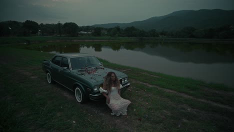 woman by vintage car by a lake at dusk