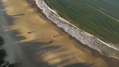 Toma-De-órbita-Aérea-De-La-Familia-Divirtiéndose-En-La-Playa-De-Arena-Durante-La-Hora-Dorada-Con-Olas-Del-Océano