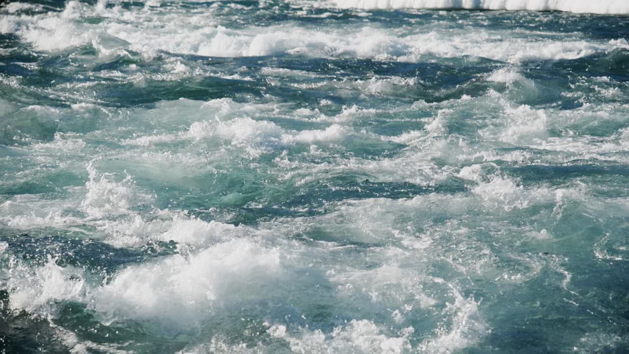 Onde potenti si infrangono sulla riva sotto il sole, creando uno spettacolo mozzafiato di acqua spumosa bianca sullo sfondo di un oceano blu intenso.