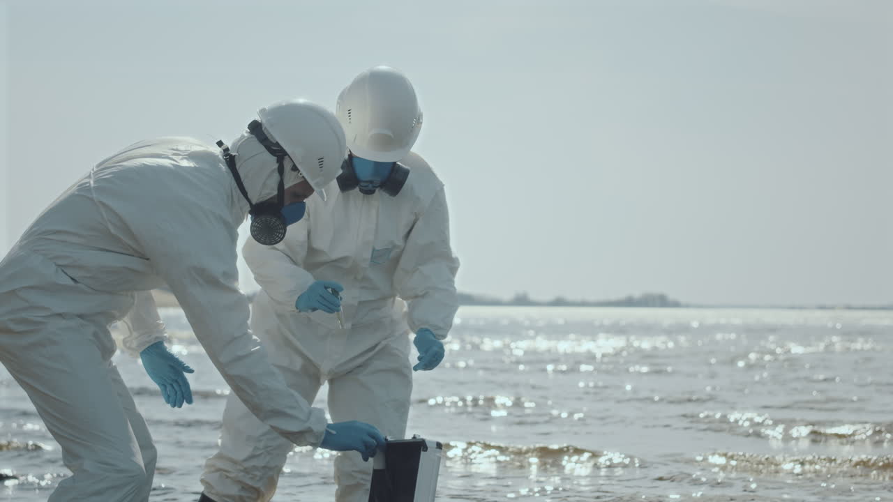 Two Ecologists in Protective Uniform Collecting Sample of Water
