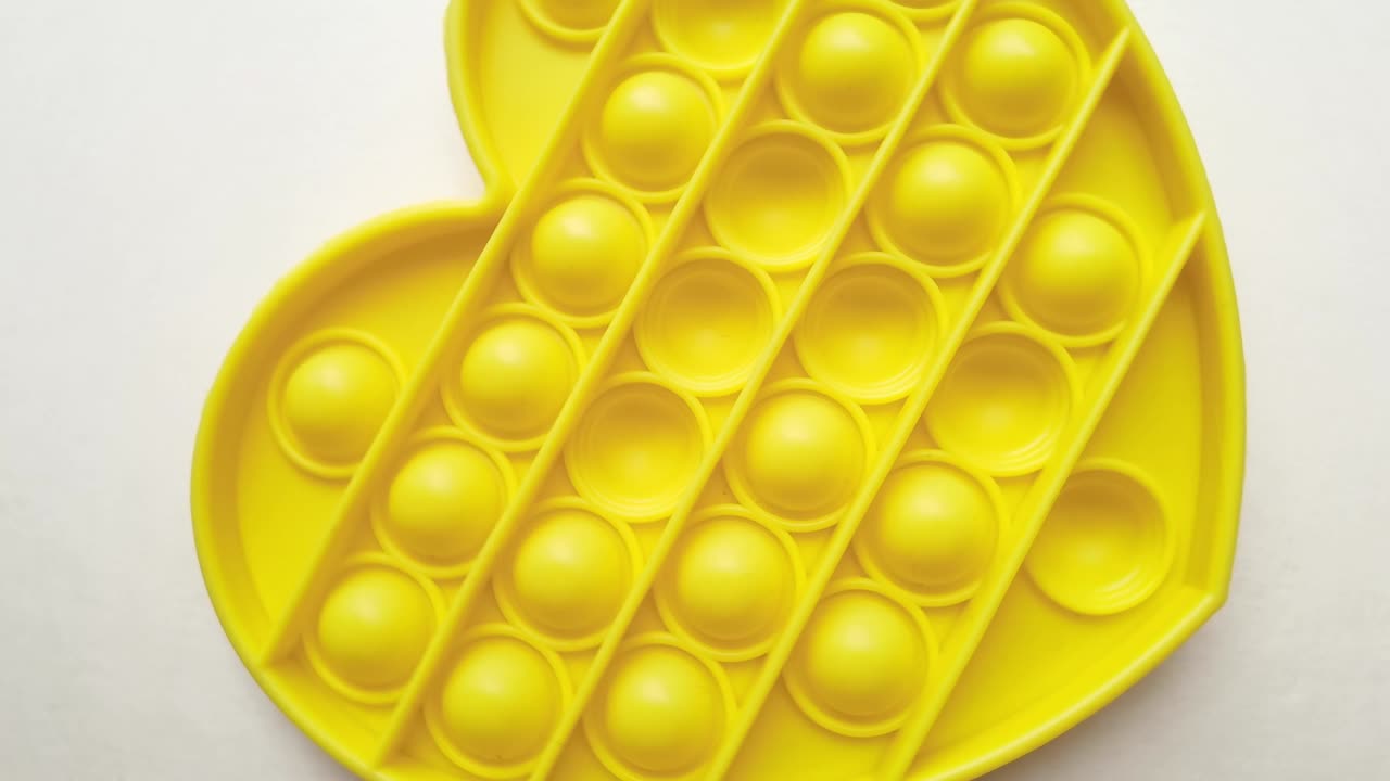 nuevo juguete para bebés. pop it juego de dedos. color gracioso. mano adulta apretando silicona redonda. cambio de forma. forma de corazón amarillo