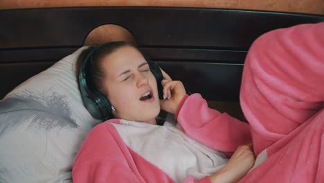 chica en pijama en la cama escucha música a través de auriculares y baila