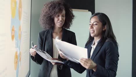 Young-beautiful-businesswomen-discussing-report-and-smiling