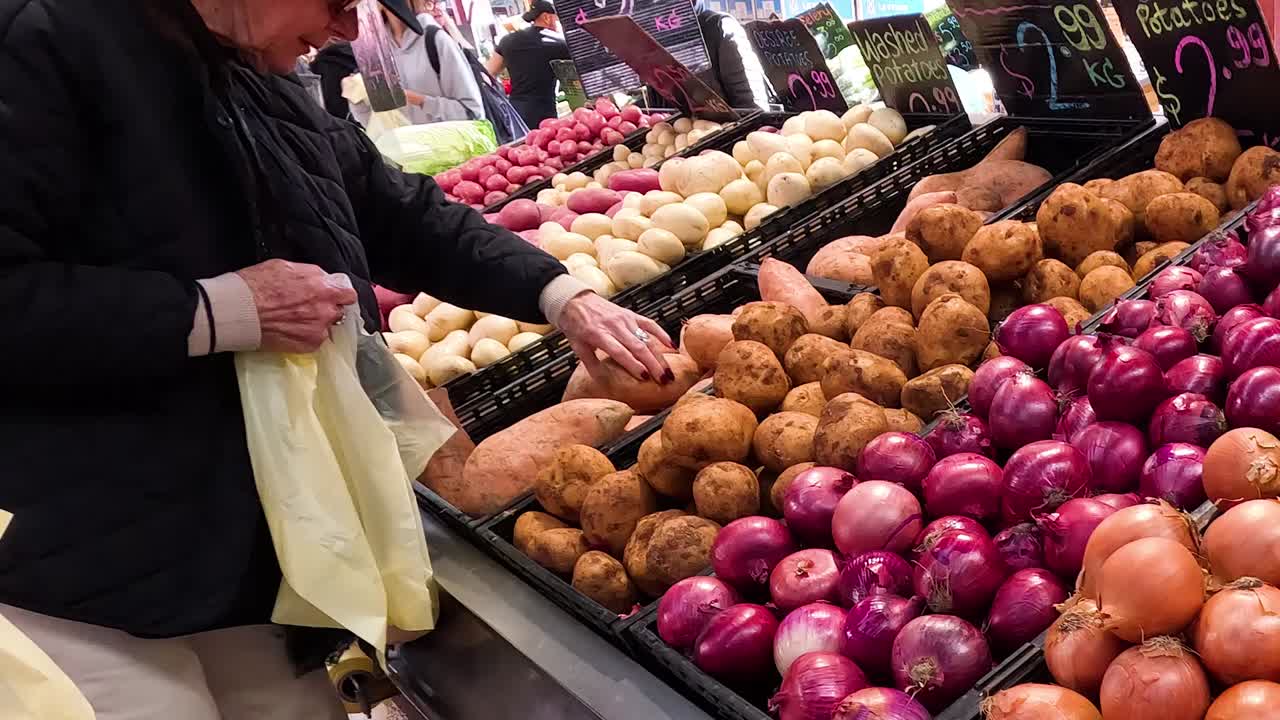 Primer plano de clientes escogiendo cebollas rojas y patatas de los contenedores en un mercado
