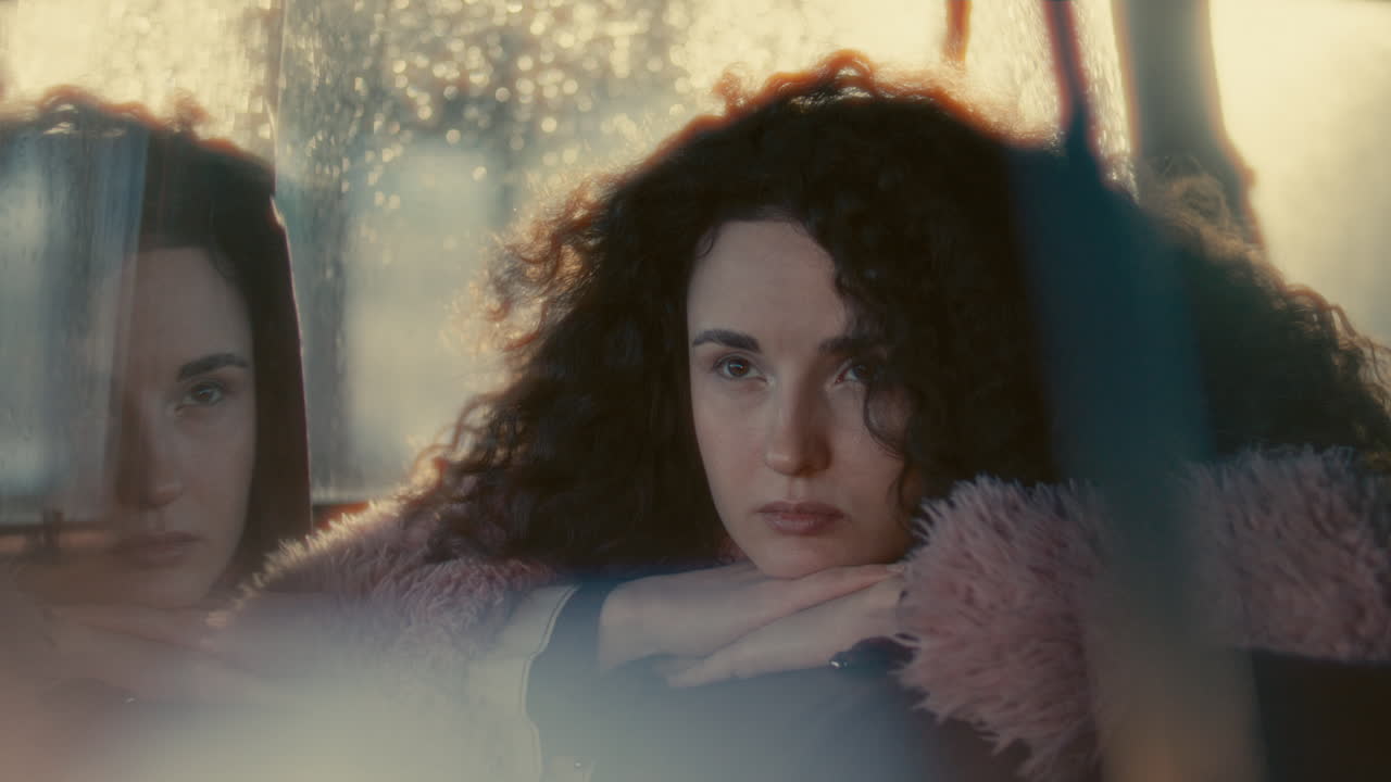 Young Contemplative Woman Sitting in Car with Rain-Streaked Windows