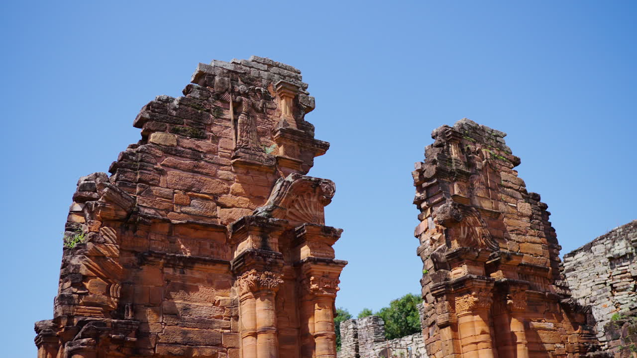 Red sandstone ruins of San Ignacio Miní Jesuit Missions showing decorative baroque carvings with clear blue sky in the background, Misiones, Argentina, slow motion panning shot