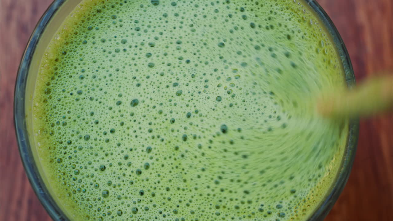 Close up of a woman mixing a matcha latte with a paper straw at a cafe