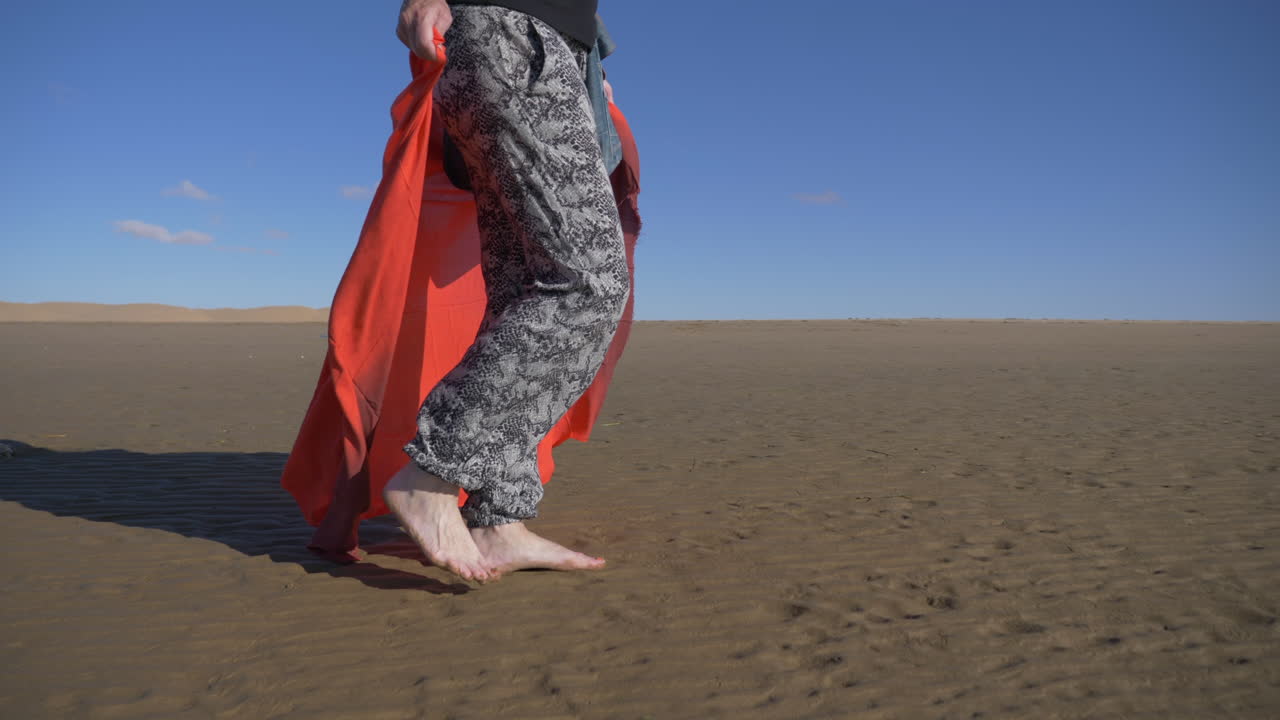 woman walking barefoot on the wet sand of Naila lagoon in Morocco holding a red fabric. khenifiss national park