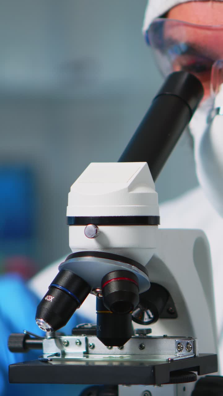 Vertical video: Close up of chemist doctor analysing virus using microscope
