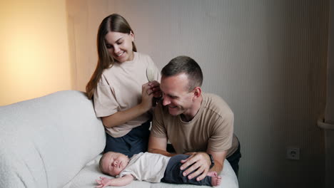 happy caucasian family of three. woman brushes hair of her husband sitting over the sleeping baby and then brushes kid's hair too.