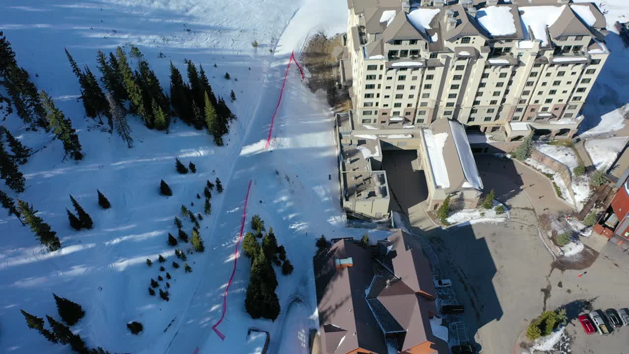 Aerial overhead view of snow-covered vacation condos tucked in pine trees, surrounded by frosty peaks and winter scenery in a peaceful mountain setting