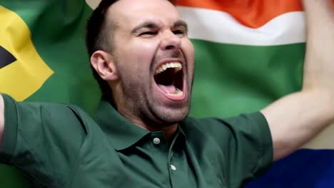 fanático sudafricano celebrando mientras sostiene la bandera de sudáfrica en cámara lenta, 4k, de alta calidad