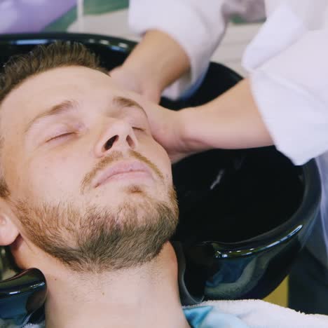 hairdresser washes mans hair in a basin