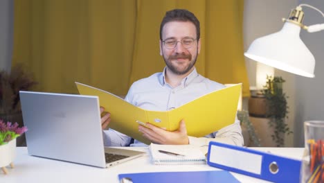 Hombre-Trabajador-De-Oficina-En-Casa-Sonriendo-A-La-Cámara-Mirando-El-Papeleo.