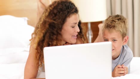 madre e hijo usando computadora portátil en la cama