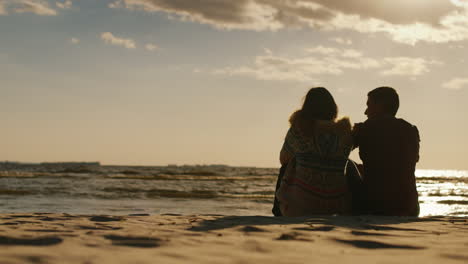 loving couple sitting on the beach at sunset cool day rear view