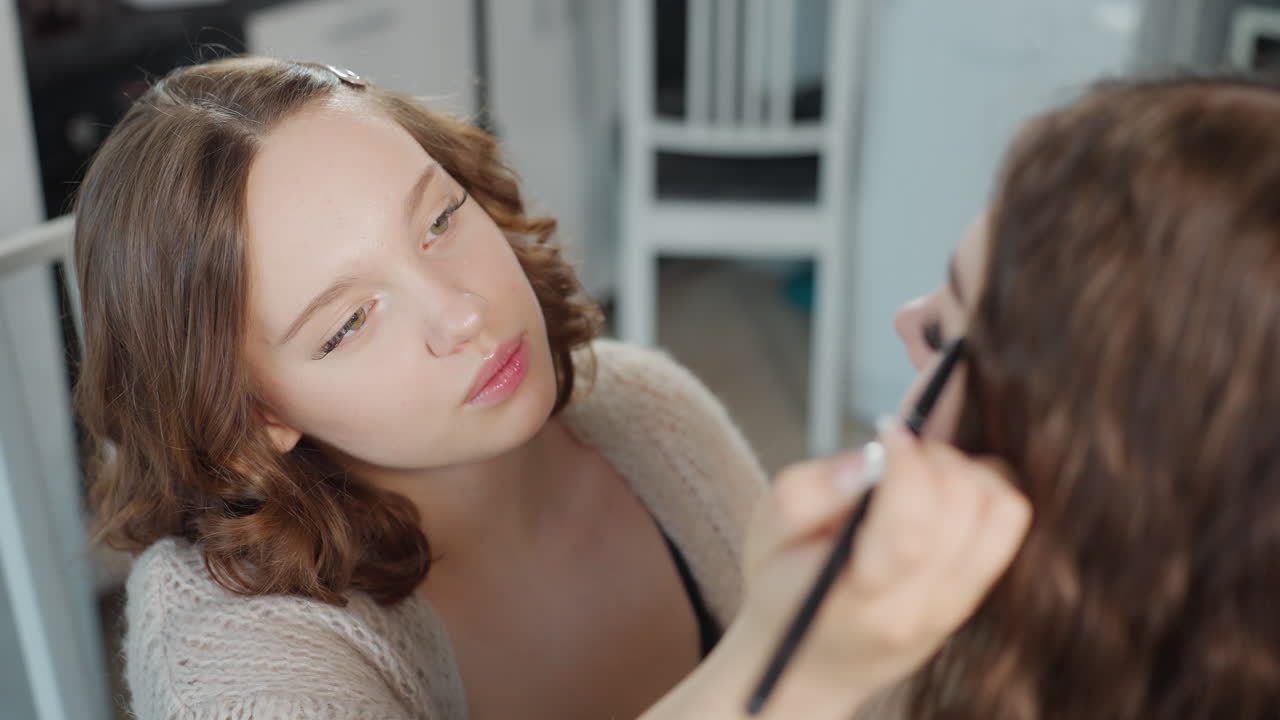 White Makeup Artist Shaping Brows With Steady Hand And Pencil, Closeup Eye Area, Careful Symmetry Checks, Mirror Reflections, Concentrated Atmosphere, Subtle Studio Lighting For Precise Grooming